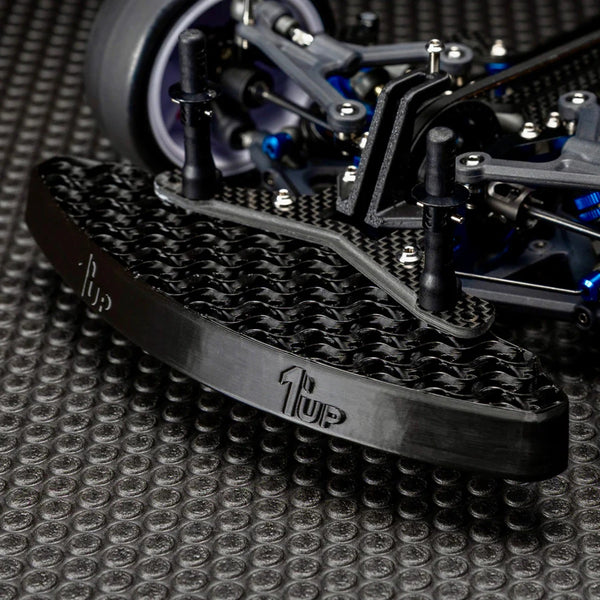 Close-up of the 1UP Racing - UltraLite Front Bumper - RC Maker SP1 mounted on a carbon fiber chassis, showcasing lightweight design and durable construction for RC racing enthusiasts.