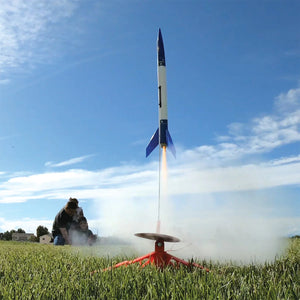 Model rocket launching into the sky with a person observing from a distance.