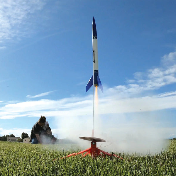 Model rocket launching into the sky with a person observing from a distance.