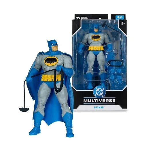 A Batman action figure posed in front of its retail packaging on a clean white background. The figure is gray and blue with yellow accents, holding a black cape-like accessory.