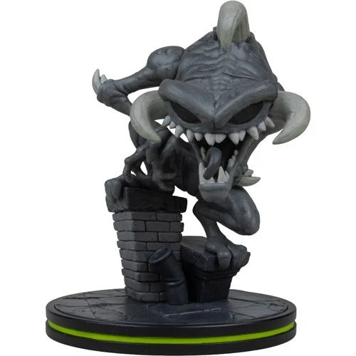 A stylized collectible figurine of a dark gray monster or goblin crouching over a brick wall on a round black base with a bright green ring, photographed against a plain white background.