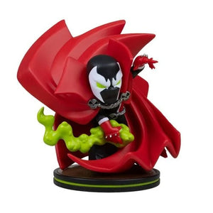 A stylized collectible figurine of Spawn with his signature red cape, black and white mask, green slime, and red gauntlets, standing on a circular display base against a plain white background.