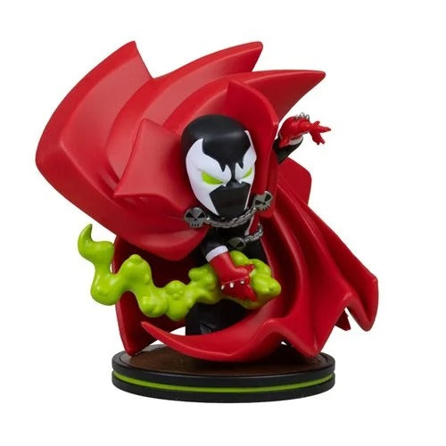 A stylized collectible figurine of Spawn with his signature red cape, black and white mask, green slime, and red gauntlets, standing on a circular display base against a plain white background.