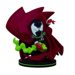 A stylized collectible figurine of Spawn with his signature red cape, black mask, green smoke, and red gloves, standing on a circular black base against a plain white background.