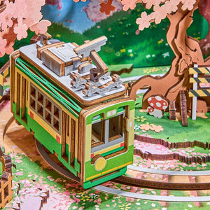 3D puzzle model of a green tram with cherry blossoms and a wooden bridge in the background