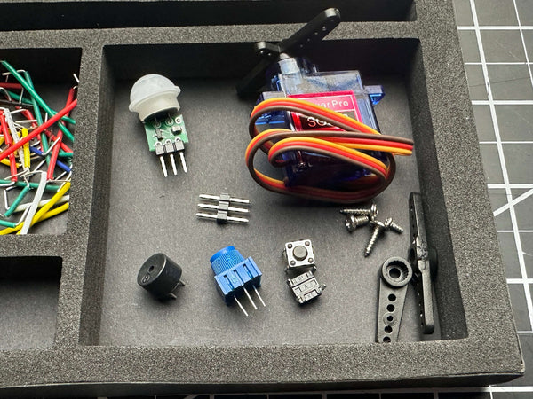 Close-up of electronic components and hobby parts including a small servo motor, push button, potentiometer, and jumper pins organized in a foam tray, supporting hands-on STEM learning with Make: Getting Started with Oxocard Connect - PDF, reflecting a veteran-owned, STEM-focused mission for enthusiasts and family-centered projects.